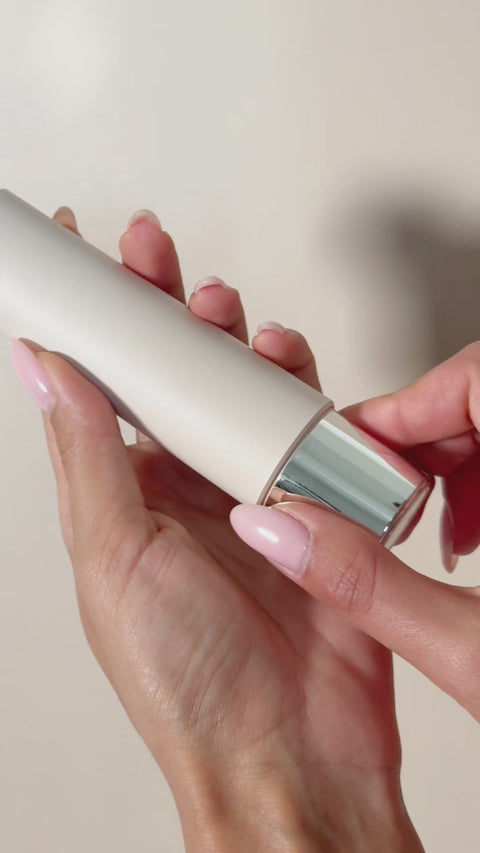 Hand holding a cylindrical electronic device with a reflective surface against a neutral background