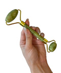 Hand holding a green jade roller on a white background