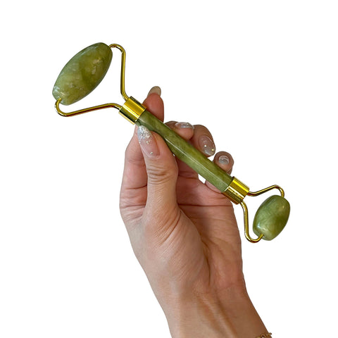 Hand holding a green jade roller on a white background