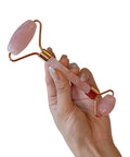 Hand holding a pink and gold facial roller against a white background