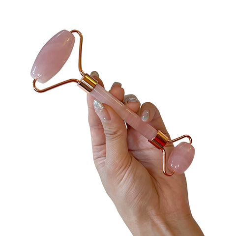 Hand holding a pink and gold facial roller against a white background