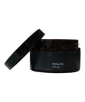 Black container of styling wax with open lid on a white background