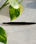 Black eyebrow pencil on a marble surface with green leaves