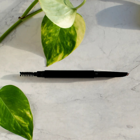 Black eyebrow pencil on a marble surface with green leaves