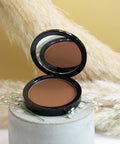 Open compact powder with a brown shade on a white pedestal against a beige background