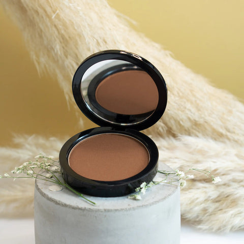 Open compact powder with a brown shade on a white pedestal against a beige background