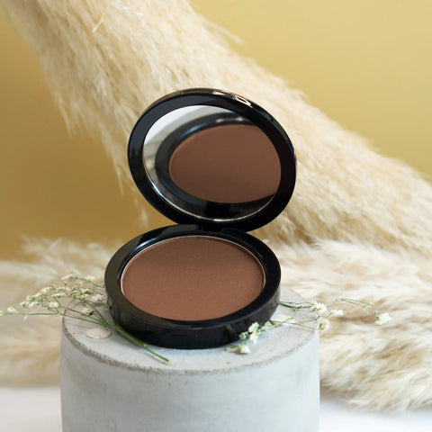 Open compact powder with a mirror on a white pedestal against a beige background