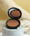 Open compact powder case with a brown shade on a textured surface with flowers.
