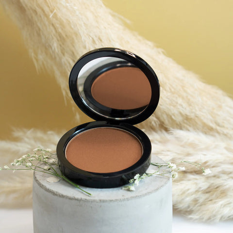 Open compact powder case with a brown shade on a textured surface with flowers.