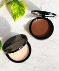 Two makeup compacts with different shades on a light surface with green leaves.