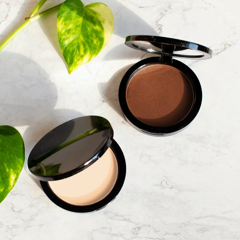Two makeup compacts with different shades on a light surface with green leaves.