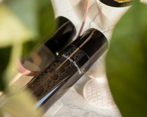 Makeup remover on a marble surface with blurred green leaves in the foreground
