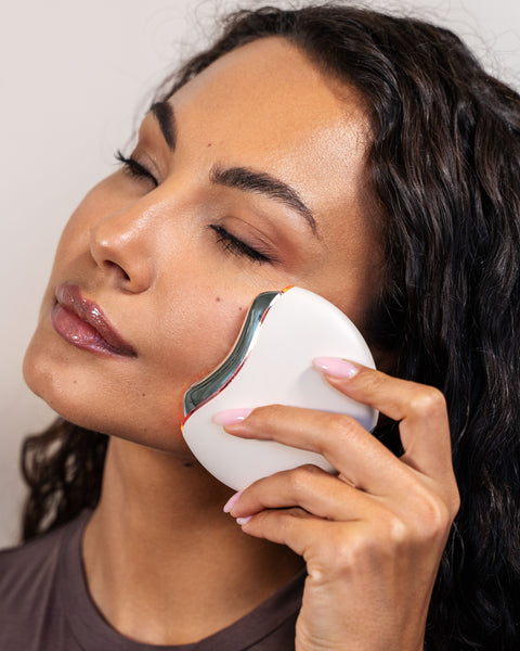 Woman using a white facial cleansing brush on her face against a neutral background