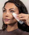 Woman applying a skincare product to her face using a applicator.