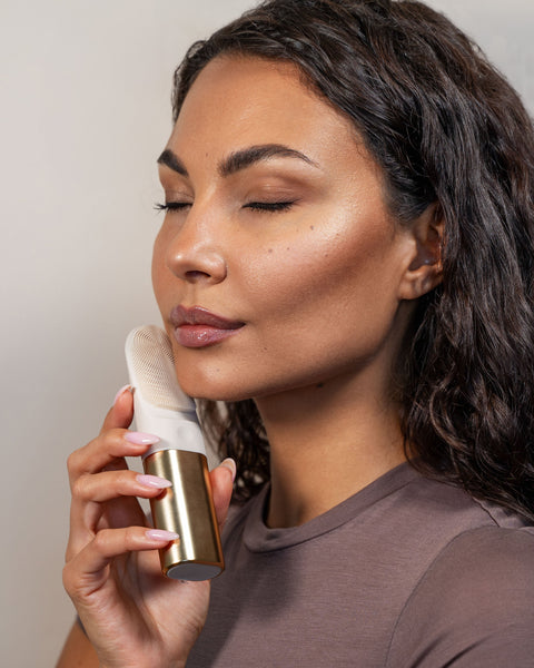 Woman using a skincare device on her face against a neutral background