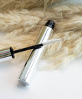 Silver mascara tube with black cap and brush on a fur surface