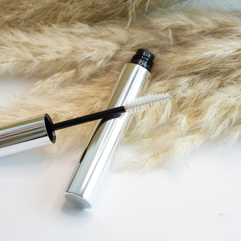 Silver mascara tube with black cap and brush on a fur surface
