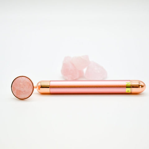 Rose gold facial roller with pink stone on a white background