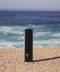Black cylindrical product on a sandy beach with ocean in the background