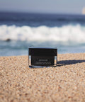 Cosmetic container labeled 'Intense' on a beach with ocean in the background