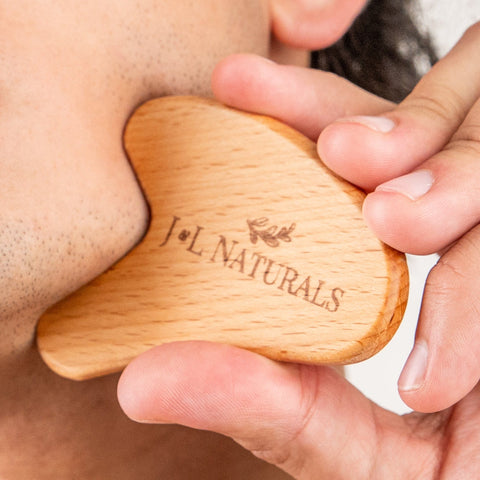 Wooden gua sha tool being used on skin with 'J&L Naturals' branding.