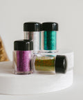 Four small jars of glitter in different colors on a white surface.