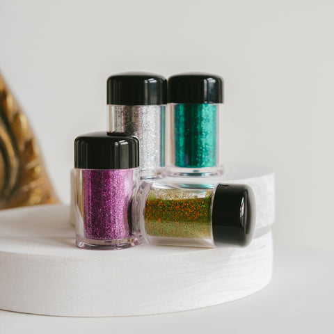 Four small jars of glitter in different colors on a white surface.