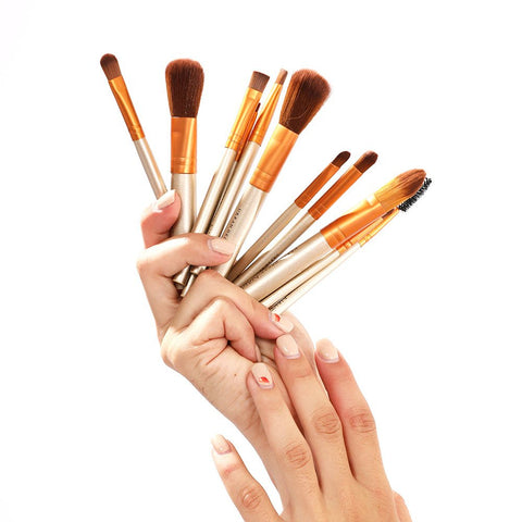 Hand holding a set of makeup brushes against a white background
