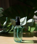 Clear spray bottle with black cap on a wooden surface with green plants in the background