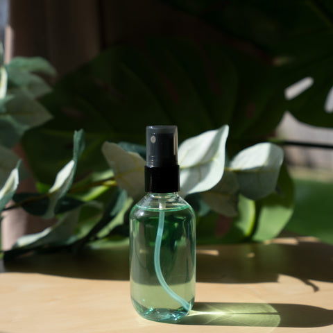 Clear spray bottle with black cap on a wooden surface with green plants in the background
