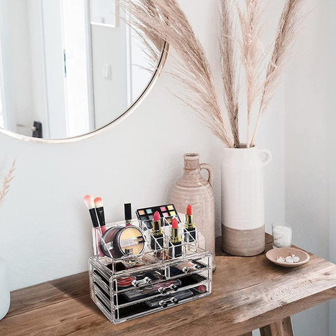 Clear acrylic cosmetic organizer on a wooden surface with makeup items, a mirror, and decorative elements.