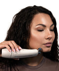 Woman using a white electronic device on her face against a neutral background