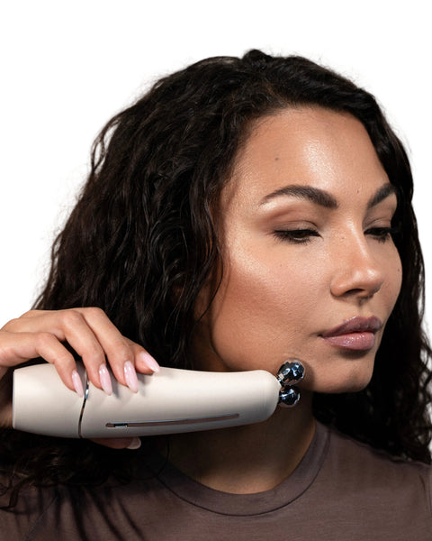 Woman using a white electronic device on her face against a neutral background